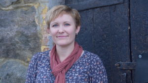 Janiina Mieronkoski handleder frivilligarbetarna i Västnyland. Personporträtt på kvinna. Bakom en svart trädörr och stenvägg. Utomhus.
