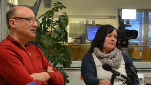 Kaj Karlstedt och Sari Wilhola. Två Ingåpolitiker sitter vid ett bord i en radiostudio. En mikrofon, papper och pennor på bordet.