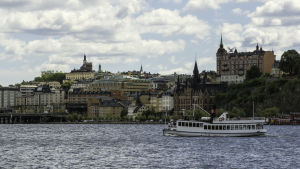 Vy över stadsdelen Södermalm i Stockholm, med Riddarfjärden och en båt i förgrunden.