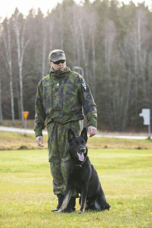 Muggy och överbåtsman Jouko Räsänen. En svart schäfer sitter framför en man i svarta solglasögon och grön kamouflageuniform.