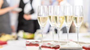 Man kan också vara med på bröllop från hemsoffan. En bricka med champagne eller mousserande vin står på ett bord. I bakgrunden synd flera personer i festkläder.