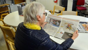 Ninni Henriksson hoppas att biblioteket får stanna kvar i Pernå också i fortsättningen. En kvinna sitter och läser en dagstidning vid ett runt bord.