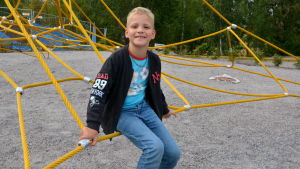 Dennis Nyblom är glad över att skolan har börjat och tycker det är roligt att leka med kompisar på eftis. En pojke sitter på en gul klätterställning.