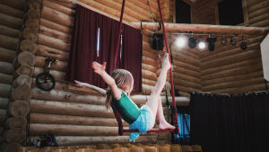 Tyttö istuu trapetsilla, kädet irti, jalka ylhäällä
