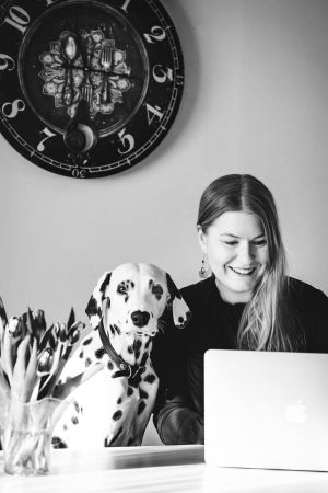 Porträtten föreställer personerna i svartvitt i sin yrkesroll. Här har producent Elin Sundell fotograferats enligt samma princip av Ian Granström. Blond kvinna ler och ser ner mot en dator. Bredvid henne sitter en dalmatin.