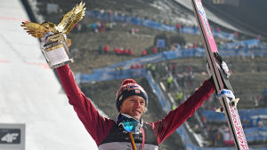 Dawid Kubacki lyfter upp pokal och skidor mot skyn.