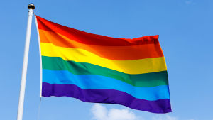 En flagga med regnbågsfärger vajar i vinden.
