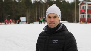 Patrick Johansson hoppas på kallare väder. En man med svart jacka och vit mössa står framför ett skidspår.