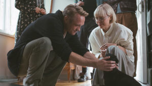 Pop hos alla. Svenska Mikael (Christian Hillborg) går hemma hos både kvinnor (Paula Vesala) och hundar. Svenska Mikael sitter på huk framför präkiga Ullas söta hund.