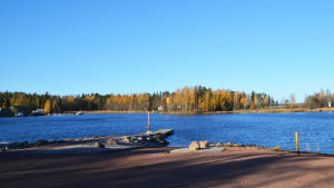 Vy från strand. Man ser en brygga vid vilken en motorbåt är fäst samt en ö mittemot.