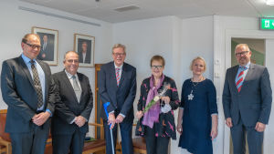 Det var stadsstyrelsens ordförande Anders Walls (SFP), ordenskommitténs ordförande Henrik Lindholm (SFP) och stadsfullmäktiges ordförande Linnéa Henriksson (SPF) som delade ut förtjänsttecknen på torsdagen (5.11). På bilden också stadsdirektör Ragnar Lundqvist och pristagarna. Fyra män och två kvinnor står i rad i kostymer och fina festkläder. De tittar in i kameran och ler. En man har kryckor.