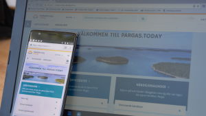 Pargas.today kan användas både med mobiltelefon och dator. En mobiltelefon lutar mot skärmen på en bärbar dator.