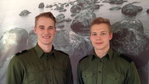 Olli Puumalainen och Janne Kinnunen från Beväringskommittéen Olli Puumalainen och Janne Kinnunen, två medlemmar i beväringskommittén vid Nylands brigad poserar framför en tavla, ett stort fotografi som föreställer hav och stenar vid strand