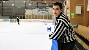 Isak Gull både spelar och dömer juniorhockeymatcher Isak Gull är ishockeydomare för yngre lag. Han står i domarskjorta utanför isen i Närpes ishall.