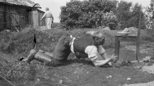En man lyfter med sin ena hand en stol som har en tung tallrik på sig. Bilden är tagen 1929 i Kungsböle, Strömfors.