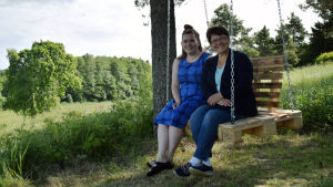 Emilia och Sara Nyberg i caféets hemgjorda kompisgunga. Emilia och Sara Nyberg sitter i en hemgjord gunga gjord av lastpallar. I bakgrunden syns grönskande ängar och skog.