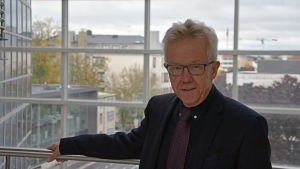 John Eriksson, professor i cellbiologi och direktör för Åbo biovetenskapscentrum. En man i kostym står framför höga glasfönster.