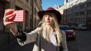 Donna (Alina Tomnikov) seisoo kadulla puhelin ojennetussa kädessään kasvojen edessä. Aurinko paistaa Donnan kasvoihin ja taustalla on autoja.