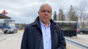 Markku Suoranta berättar att coronaåret varit tufft för Österbottens cancerförening men tack vare en insamling som är på slutrakan kommer cancerföreningen att kunna verka också i framtiden. En man med glasögon och mörkblå ytterrock står utomhus och håller ett munskydd i ena handen och tittar in i kameran. I bakgrunden syns ingången till ett sjukhus.