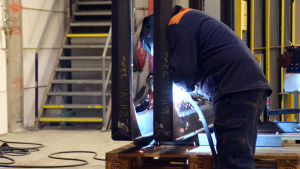 SBA Interior levererar produkter till andra aktörer inom metallbranschen. Här svetsas ett föremål till en stockbil. En person svetsar på ett föremål i en fabrikslokal.