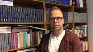 Pekka Lindqvist, universitetslärare i exegetik och judaistik. Jukka Lindqvist står framför bokhyllor.
