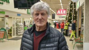 Hans Östman. Man i grått hår med vinterjacka tittar in i kameran. Han står inne i butiksmiljö.