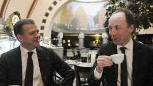 Debatten mellan oppositionsledarna hölls på ett café i Helsingfors. Petteri Orpo och Jussi Halla-aho dricker kaffe och ler mot varandra.