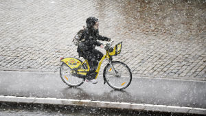 Till skillnad från de andra elsparkcyklarna hyr man HRT:s sparkcyklar från en station, precis som stadscyklarna. Nainen pyöräilee lumisateessa Helsingissä.