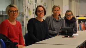 Fyra kvinnor sitter bakom bord i ett klassrum.