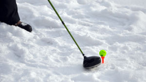 En färggrann golfboll passar bra mot den vita snön. En golfklubba som ska slå en golfboll. Underlaget är snö.