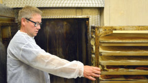 Ben Henriksson tar ut den rökta fisken ur ugnen. En man tar ut en last plåtar ur en rökugn.