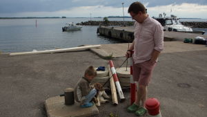 Markus Lampenius tillsammans med sin son och familjens hund. en pappa med sin son och hund vid en båthamn