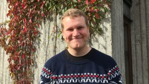Svensken Kristofer Dahlgren. Kristofer Dahlgren framför grå vägg med röda blommor.