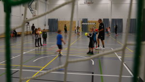 Det finns många aktiva inom Akilles handboll. Barn spelar handboll inne i en idrottssal.Kastar en gul boll till varandra.