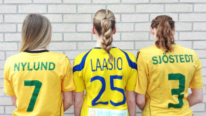 De här tjejerna har alla börjat spela handboll som barn. Tre tjejer står med ryggen mot kameran, iklädd sina speltröjor.
