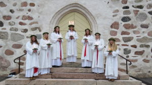 Folkhälsan i Tenala har i år låtit sy upp vita kappor i fuskpäls eftersom den ursprungliga planen var att hålla luciakröningen utomhus. Lucia med sex tärnor ute på kyrktrappa. De är klädda i vita kappor av fuskpäls.