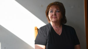 Jelena Vassiljeva sitter på en stol intill en vägg, skarpt solljus belyser hennes arm.