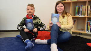 Aron Aaltonen och Wilma Kostiainen tycker om boken om pärlfiskande Miranda. Aron Aaltonen och Wilma Kostiainen håller upp var sin bok, de sitter på golvet.