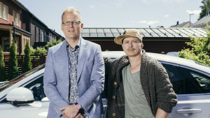 Luottomiehen Juhis (Kari Ketonen) ja Tommi (Antti Luusuaniemi) seisovat vierekkäin vaaleaan autoon nojaten kotipihassaan katsoen kameraan.