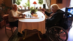 Arkivbild. En äldre man sitter och spelar spel med en äldre kvinna som sitter i rullstol.