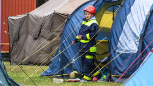 Brandkårslägret ger medlemmar från olika brankårsföreningar en chans att träffas och umgås. Pojke i brandkårsdräkt framför ett tält.