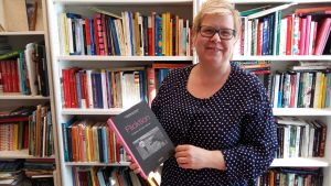 Maria Österlund med en av de nyare böckerna om flickforskning. En bok vars titel anspelar på orden flickor, fiktion och friktion Maria Österlund poserar med boken Flicktion i handen.