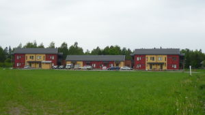 Sjundeås hjärta ska bli ett tätt och miljövänligt centrumområde till exempel för tågpendlare. Tre rödgula hus med träfasad, en grön gräsplan i förgrunden.