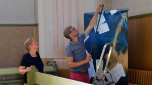 Ilar Gunilla Persson får hjälp med att hänga upp fotografierna i kyrkan. Ilar Gunilla Perssons fotografier hängs upp i Lovisa kyrka