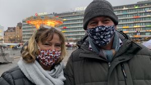 Lena Sahlström och Paul Wilkinson tänker köpa sina julklappar lokalt i Vasa. Kvinna och man med munskydd tittar in i kameran. I bakgrunden Vasa torg.