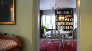 Biblioteket sett från Gröna rummet. I Gröna rummet hänger porträtt på alla författare som har bott i huset. På bilden synns ett bord och stolar samt en bokhylla medböcker. Bilden är tagen från dörröppningen i ett rum med gröna väggar in mot biblioteket.