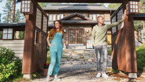 Nainen ja mies seisovat japanilaistyylisellä portilla, taustalla näkyy piha ja talo.