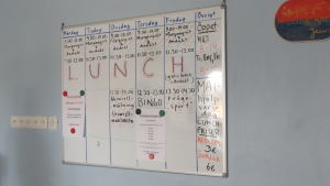 De omtyckta luncherna, bingon och frågesporterna är lagda på is i Vänstugan i Ekenäs. En whiteboardtavla med schema över program på olika veckodagar. Bland annat bingo, frågesport, morgongröt och andakter plus lunch och mathjälp.