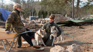 Milla och Markku Vahtila har uppnått många drömmar, och sett andra gå i kras. Att göra saker tillsammans är viktigt för dem. En man och en kvinna pausar från byggarbete, mannen lutar mot en skottkärra och kvinnan gullar med två huskyhundar.
