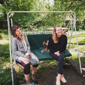 Enligt Stella Tiisala (till vänster) och Kristiina Välimäki finns det många fördelar med att bo i ett trähusområde. Alla bor nära varandra, vilket gör vardagen lättare eftersom barnen fritt kan gå från hus till hus. Man hör barnens lek och prat eka mellan husen, och dessutom kan de vuxna hojta åt varandra och gå på kaffe. Kaksi naista istuu pihakeinussa vihreällä pihalla Paraisten Vanhalla Malmilla.